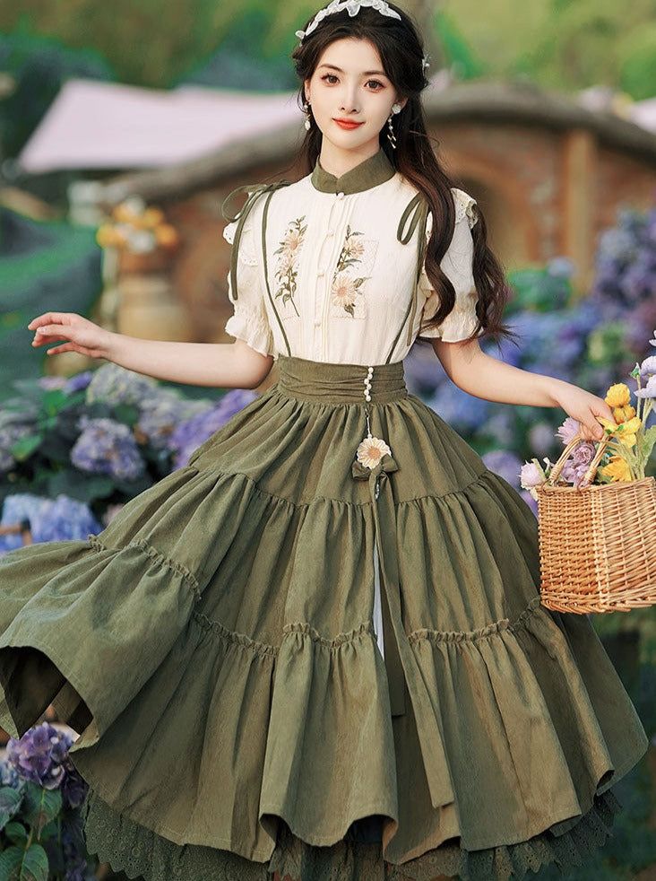 a woman in a vintageinspired outfit poses in a garden. she is wearing a white blouse with embroidered flowers, a long green tiered skirt, and a matching green ribbon belt. she is holding a wicker basket of yellow and purple flowers. the background is a blur of green foliage. the image is lit with soft, natural light, giving it a romantic and dreamy feel.