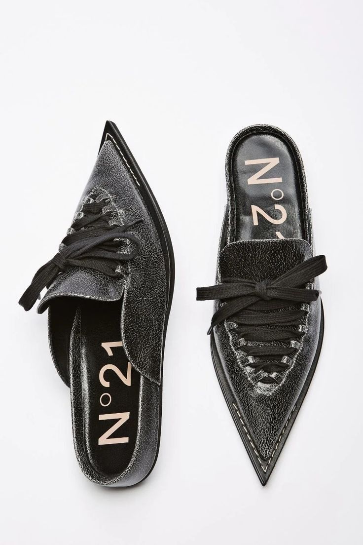 a pair of black n°21 women's mules with pointed toes. the shoes are made of textured leather and have a laceup detail on the vamp. the brand's logo is visible on the insole of each shoe. the shoes are styled as a pair, and are positioned against a white background.
