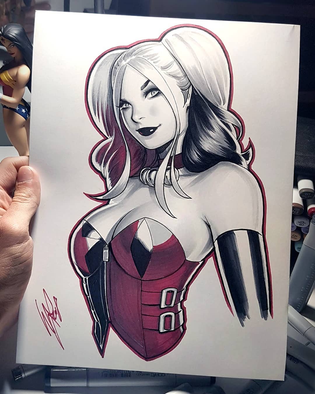 a handdrawn illustration of harley quinn in red and black ink, wearing a red and black jesterinspired costume.  her signature pigtails are pulled back into a loose ponytail, and she is looking at the viewer with a playful smile. the drawing is signed and dated by the artist.