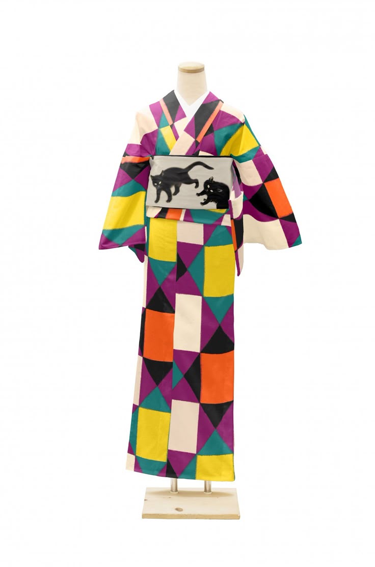 a kimono displayed on a mannequin with a colorful geometric pattern of triangles and squares. it features an obi sash with black cat designs. the colors include purple, yellow, orange, white, teal, and black.