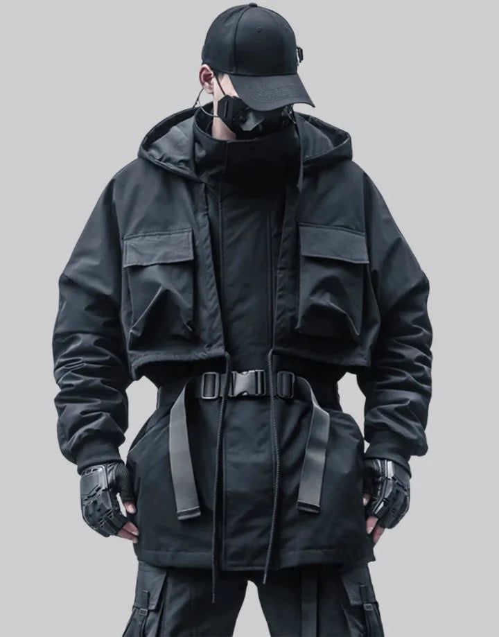 a man poses for the camera in an allblack outfit. he is wearing a black hooded jacket with large pockets, a black mask, black gloves, and black pants. the man has a black cap on his head and is standing in a gray studio space.