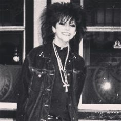 a young woman with short black hair is wearing a leather jacket with a cross necklace. she has a serious expression on her face and looks directly at the camera. the image is in black and white.