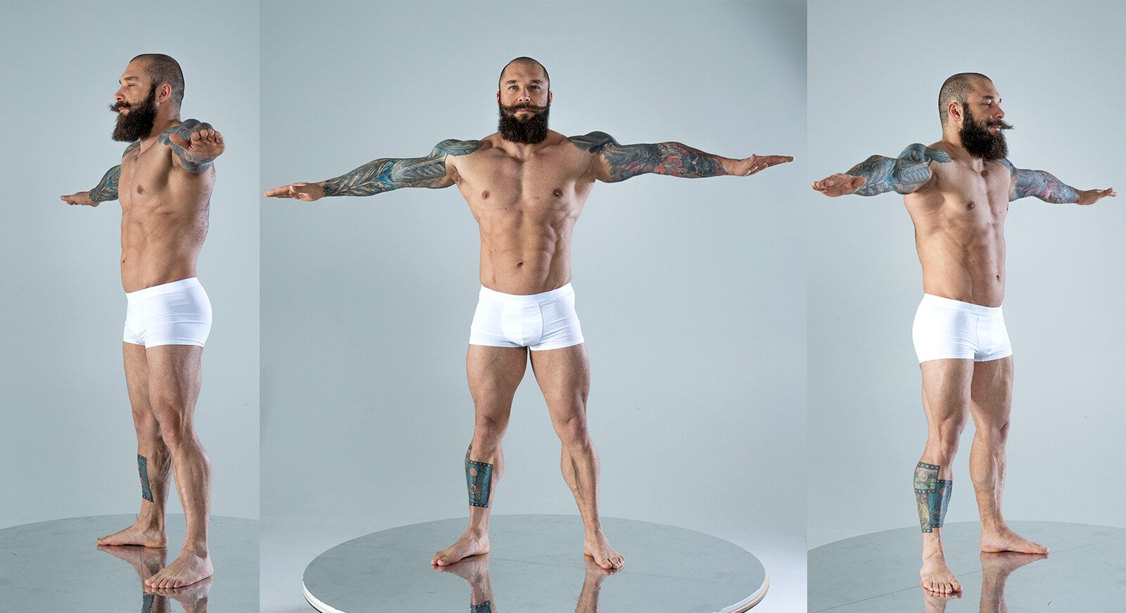 a muscular, tattooed man with a beard is posing in white underwear on a reflective floor in a studio. the man is facing forward with arms spread out in the middle image, facing left in the left image and facing right in the right image.