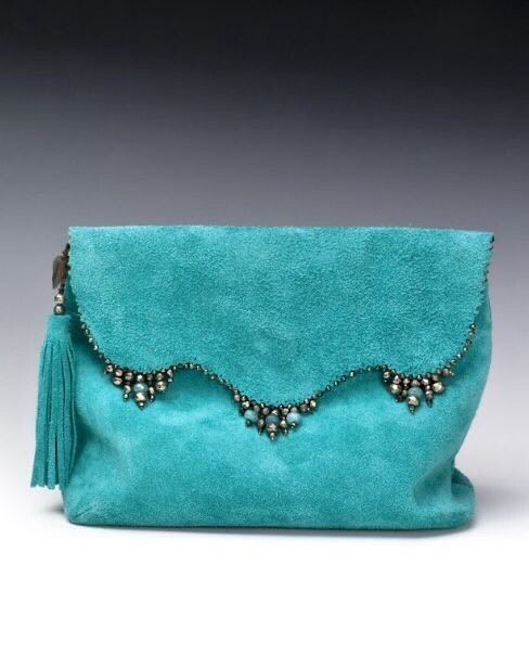 a teal suede handbag is displayed against a dark background. the bag features a decorative flap with beaded accents along the scalloped edge. a tassel hangs from the side of the bag.