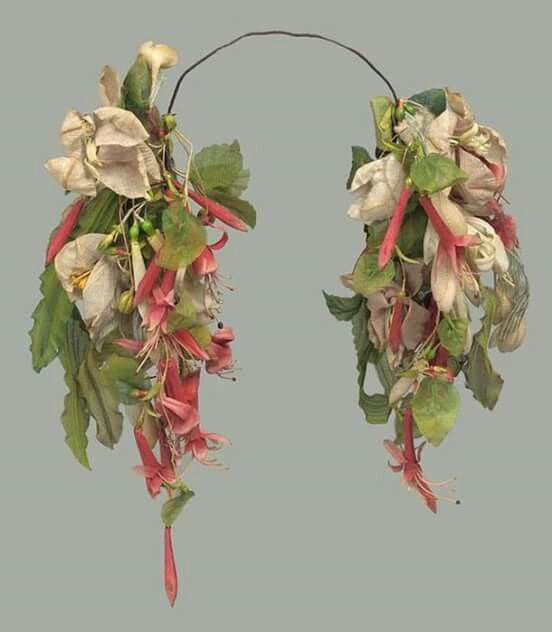 a floral headpiece featuring fuchsia and white flowers with green leaves, attached to a wire frame. the flowers are arranged in a cascading fashion, creating a decorative and potentially vintage or antique look.
