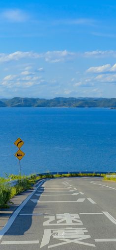 a winding road curves upward, leading towards a breathtaking view of a serene blue lake nestled against a backdrop of rolling mountains under a sunny sky. traffic signs stand sentinel at the road's edge, hinting at the journey ahead.