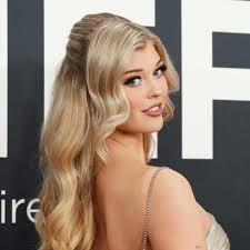 a portrait of loren gray with blond wavy hair in a half updo, looking over her shoulder wearing an evening gown at an event.