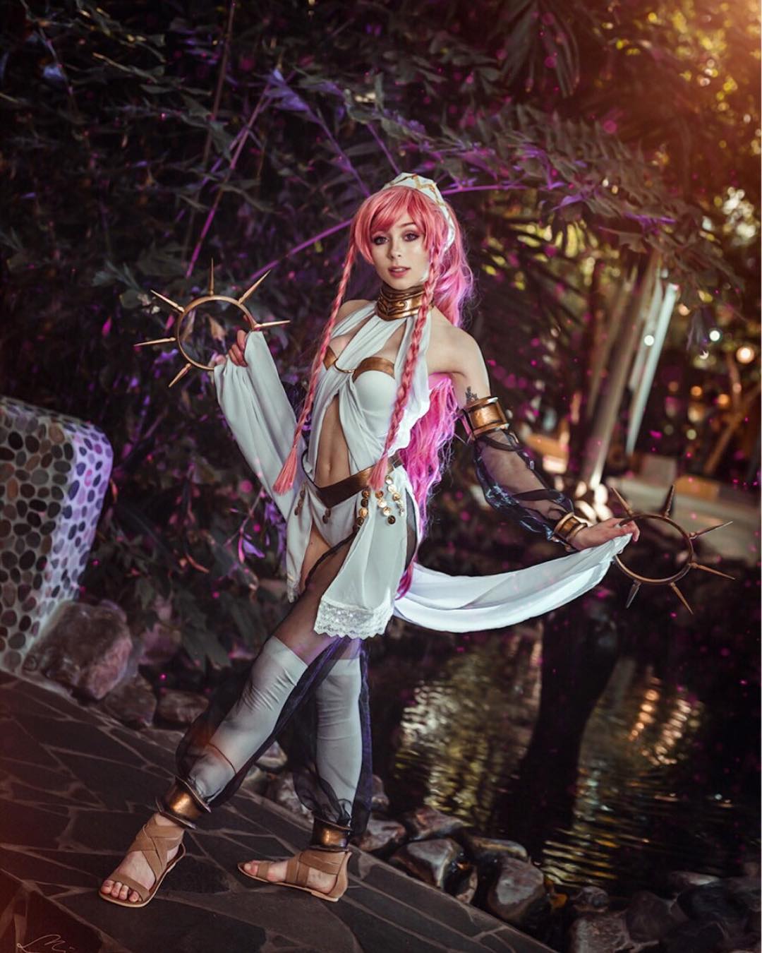 a captivating cosplay photograph showcases a female cosplayer dressed as a fantasy character, possibly inspired by anime or a video game. she has long, bright pink hair and wears a white and black costume with ornate details, including metallic accents on the chest piece and armguards. the outfit is suggestive of a magical warrior or goddess. she holds two decorative, ringshaped weapons, adding to the mystical ambiance.  the setting is a picturesque outdoor location at night, with a tranquil pond and rock formations in the background. the lighting and postprocessing enhance the overall fantastical effect.  the cosplayer's pose and expression are confident and expressive, drawing attention to the meticulously crafted costume.