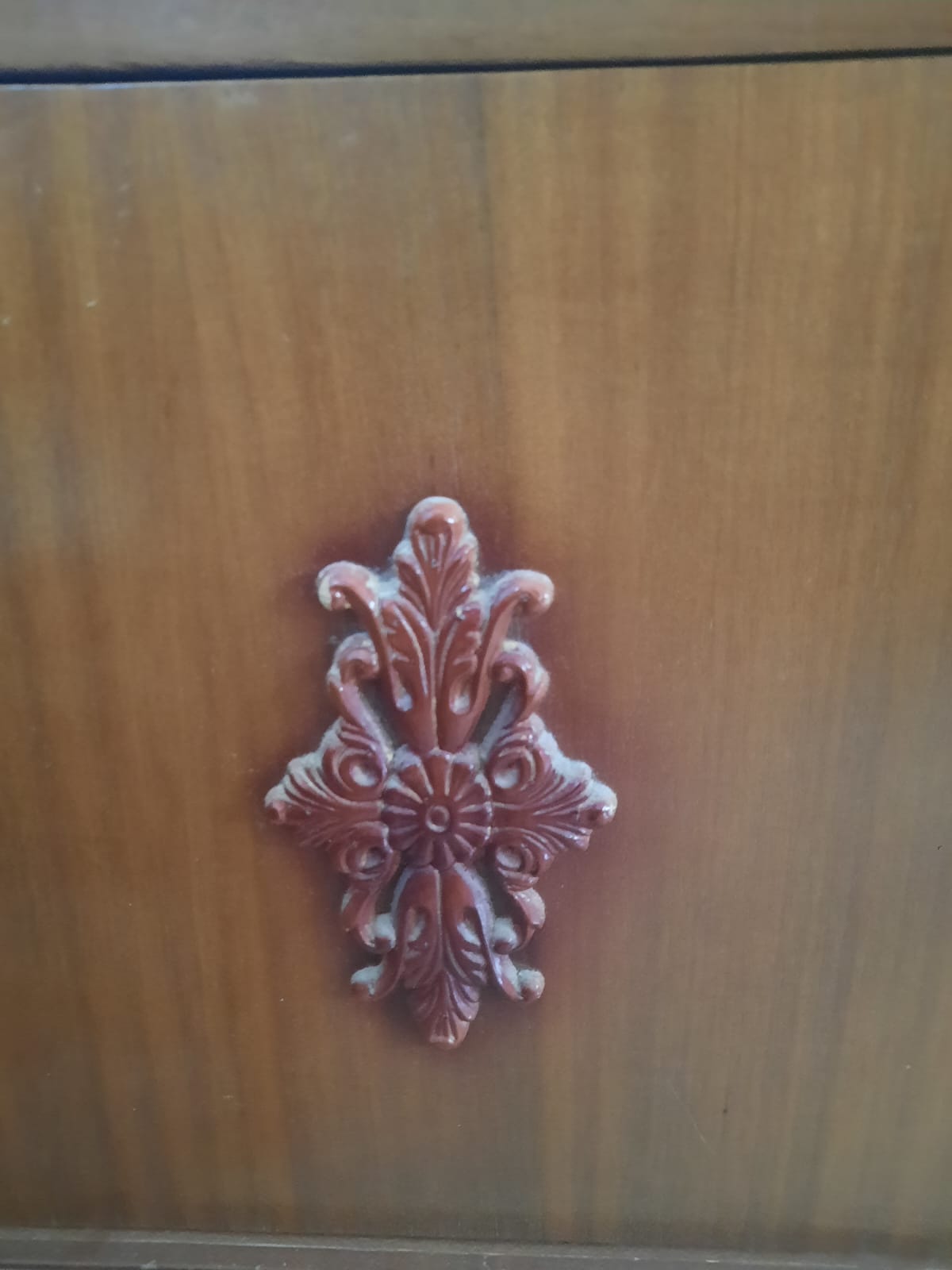 closeup of a wooden drawer with a carved floral design in the center. the drawer is made of light brown wood with visible wood grain. the floral carving is a darker shade of brown and features a flowerlike center surrounded by intricate leaf and swirl patterns.