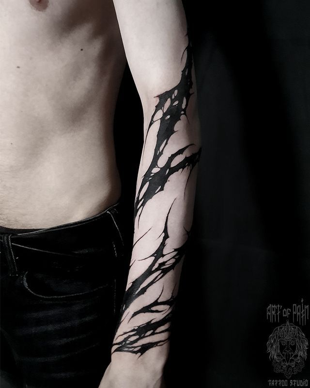 a close up image of a person's arm, with a black ink abstract tattoo going from their wrist up to their elbow. the tattoo is done in a black and white minimalist style, with sharp lines and geometric shapes. the image is in focus. the lighting is bright, with the person's skin looking smooth and clear.  the person is wearing black jeans.  the studio name, "art of pain," is visible at the bottom right of the image.
