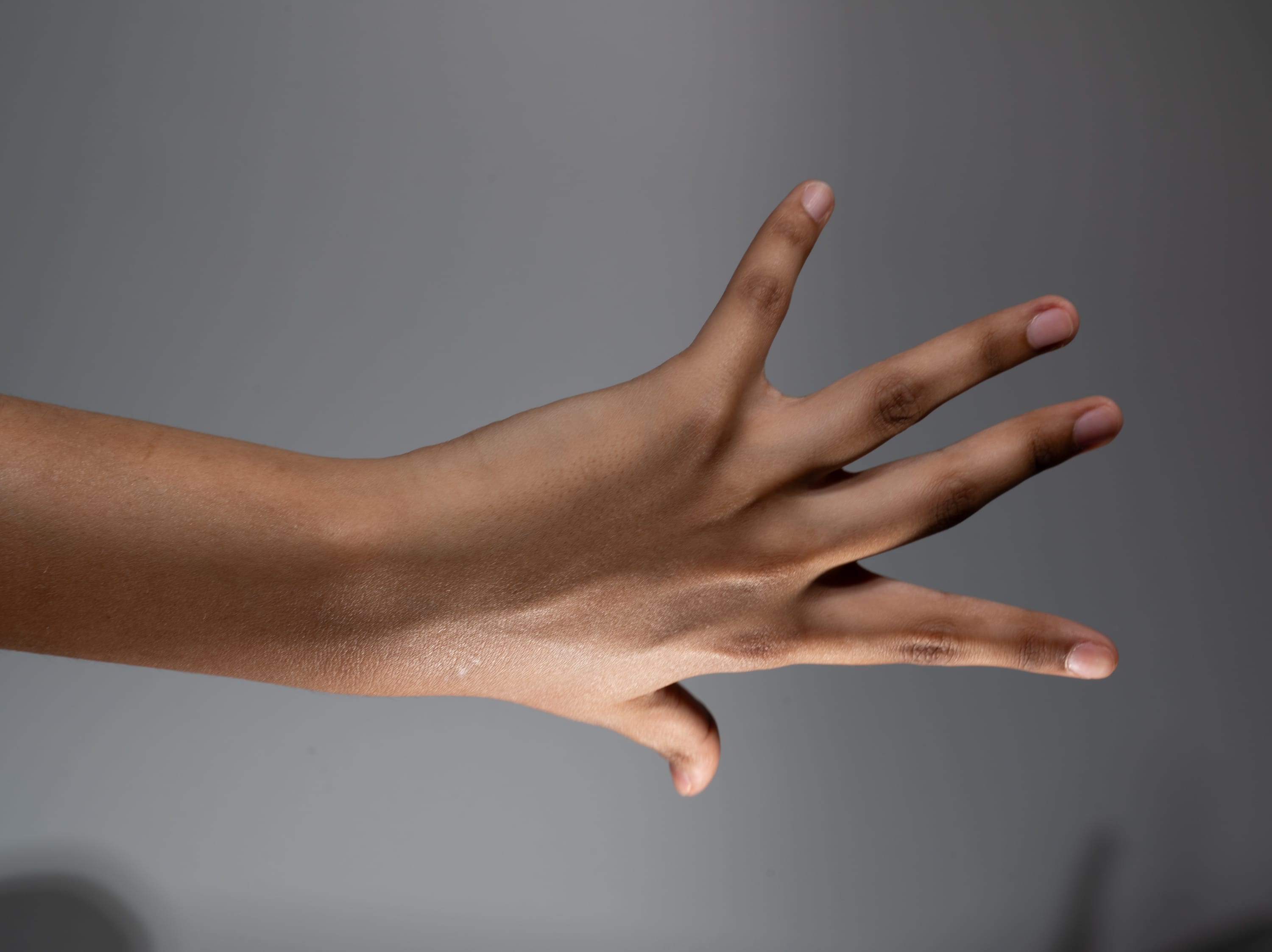 an image of a person's hand with shimmering brown skin is extended towards the camera against a gray background. the hand is open with fingers slightly spread, illuminated by soft, artificial light.