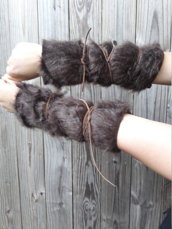 a person is wearing fur arm guards on each arm, secured with leather cord. the arm guards are dark brown fur. the background is a wooden wall.