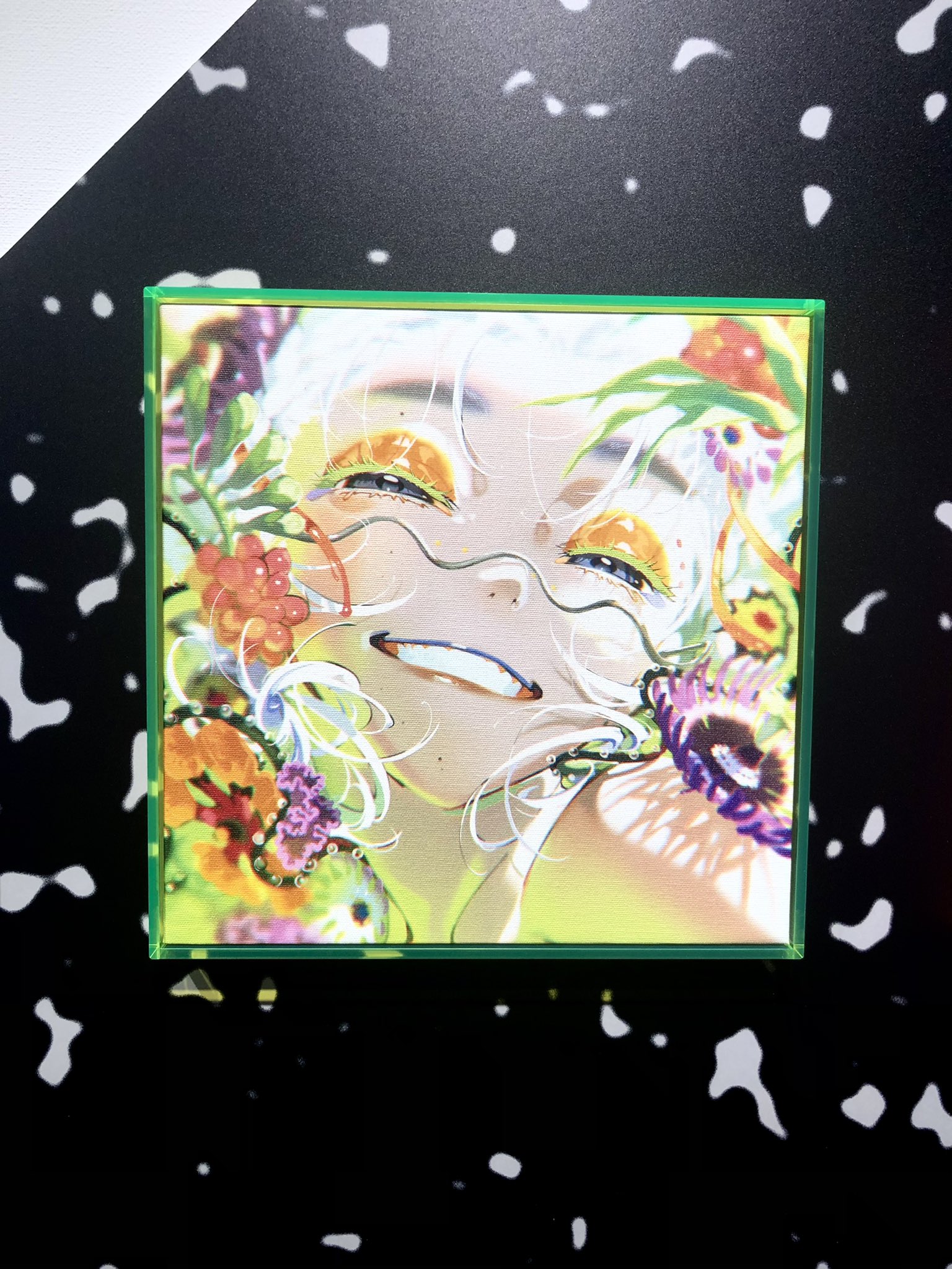 the image is a digital illustration of a smiling person with white hair. the person is surrounded by colorful flowers on a white background. the illustration is framed by a green border. the background behind the frame is black with white speckles.