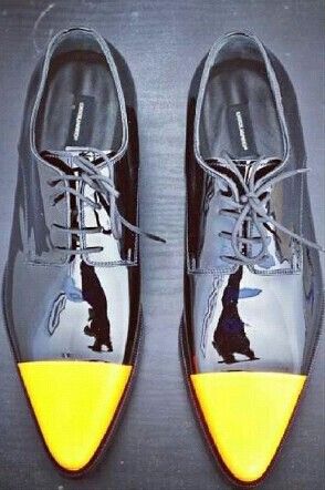 the image shows a pair of men's dress shoes.  the shoes are black patent leather oxfords with a distinctive yellow cap toe. they are meticulously polished and have a classic, elegant design. the shoes are positioned against a dark gray background, allowing their sheen and color contrast to stand out.  the viewpoint is a slightly overhead shot, giving a clear view of the shoes' details.