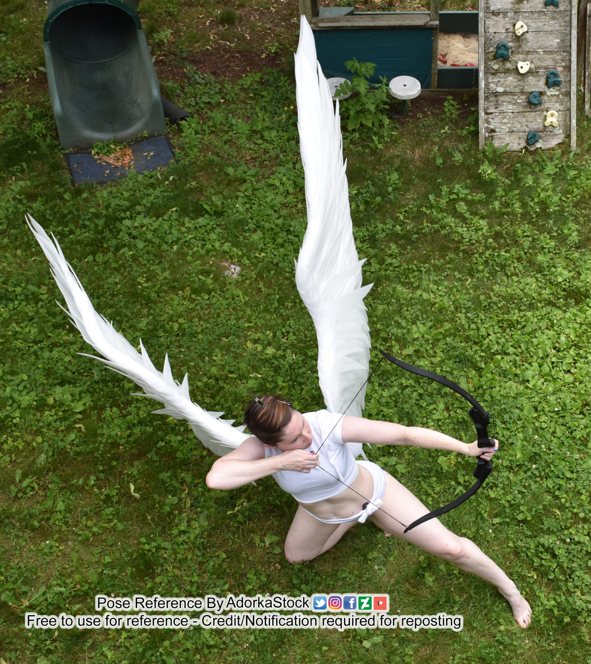 a woman with angel wings and holding a bow and arrow is shooting a target. she is in an outdoors setting on a grassy area.  this is a pose reference image, which can be used for art, animation, and other creative purposes.