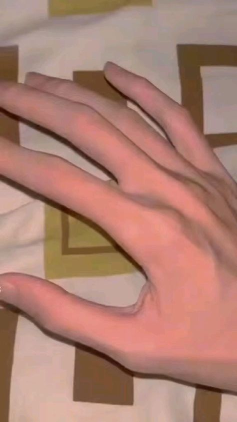 a closeup image of a slender hand with long fingers resting on a bed with a geometric patterned sheet. the lighting is soft, giving the hand a delicate and almost ethereal appearance. the overall aesthetic of the image is soft and muted, with a focus on the beauty of the hand and the textures of the fabrics.