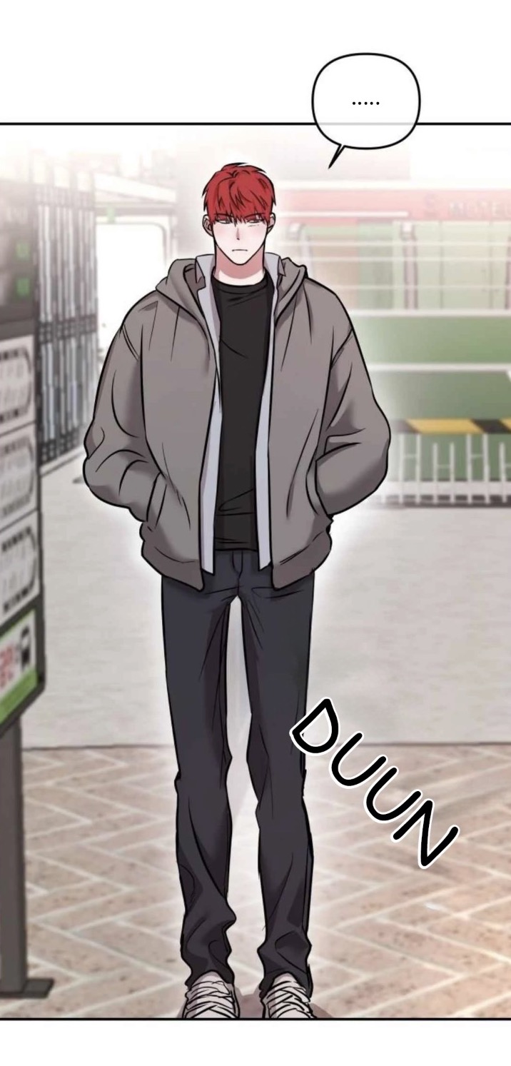 the image is a panel from a korean webtoon or manhwa. it depicts a young man with red hair, wearing a gray hoodie and black pants, standing in a hallway or inside a store. he has a neutral expression on his face. the background suggests a shopping mall or similar indoor setting. the style is typical of a webtoon or manga, with clear line art and shading. there is a sound effect "duun" added to the image.  the overall mood is quiet and somewhat mysterious.