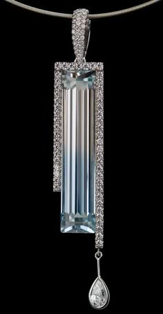 a closeup shot of a silver pendant with a large aquamarine gemstone set in a diamond frame. the pendant is attached to a silver chain. the image is lit from the front, highlighting the sparkle of the diamonds and the blue of the aquamarine. the pendant hangs against a dark background.