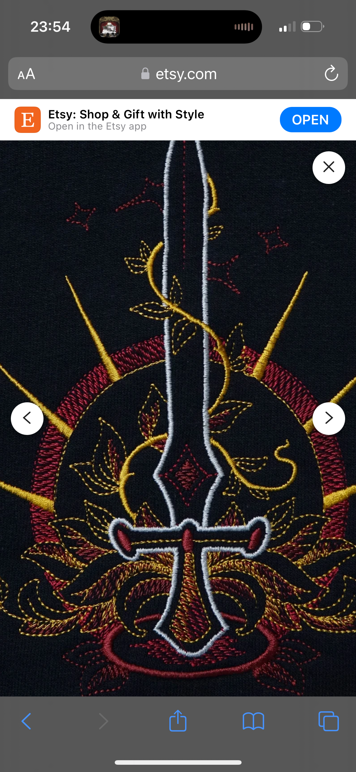 a closeup shot of an intricate embroidery design on a black fabric. the design features a stylized sword surrounded by floral motifs. the sword is outlined in white and filled with a gradient of red and gold, with intricate detail on the blade and hilt. the floral motifs are outlined in yellow gold and filled with white, with intricate detail on the leaves and petals. the background of the design is a black fabric, which allows the colors of the embroidery to pop.  the photo was likely taken on a phone with a digital app.