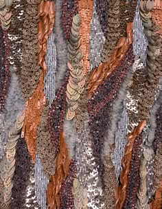 close up view of a brown, silver, and gray patterned fabric with beaded and sequined accents. the fabric has a layered and textured effect, with the sequins creating a shimmering effect. the image highlights the intricate detail of the fabric, showcasing the craftsmanship and beauty of the material.