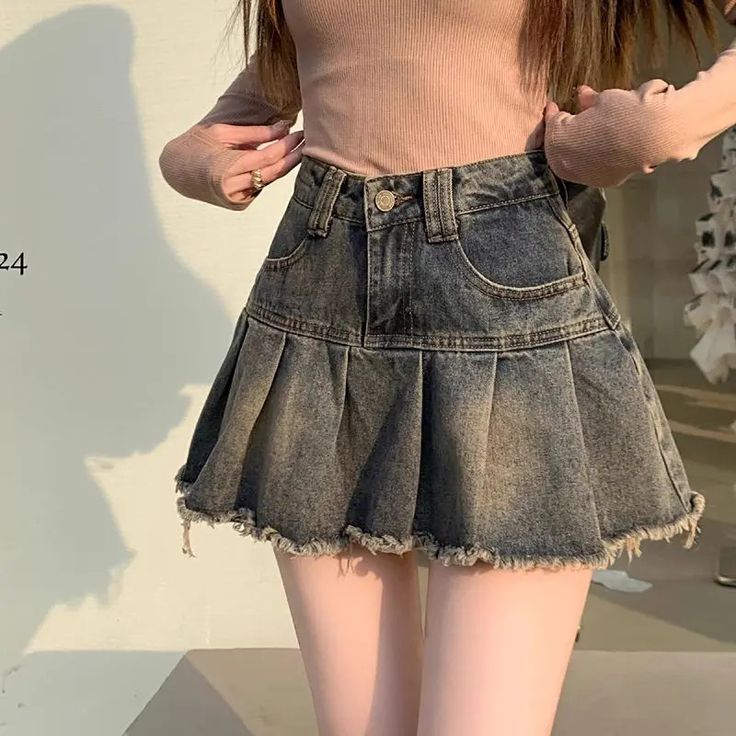 a young woman is wearing a pink top and a denim skirt. the skirt is pleated and has a frayed hem. she is standing with her legs slightly apart, showing off the skirt. the skirt is very short and reveals her legs.  the woman's hair is long and straight. the photo is taken in a casual setting.