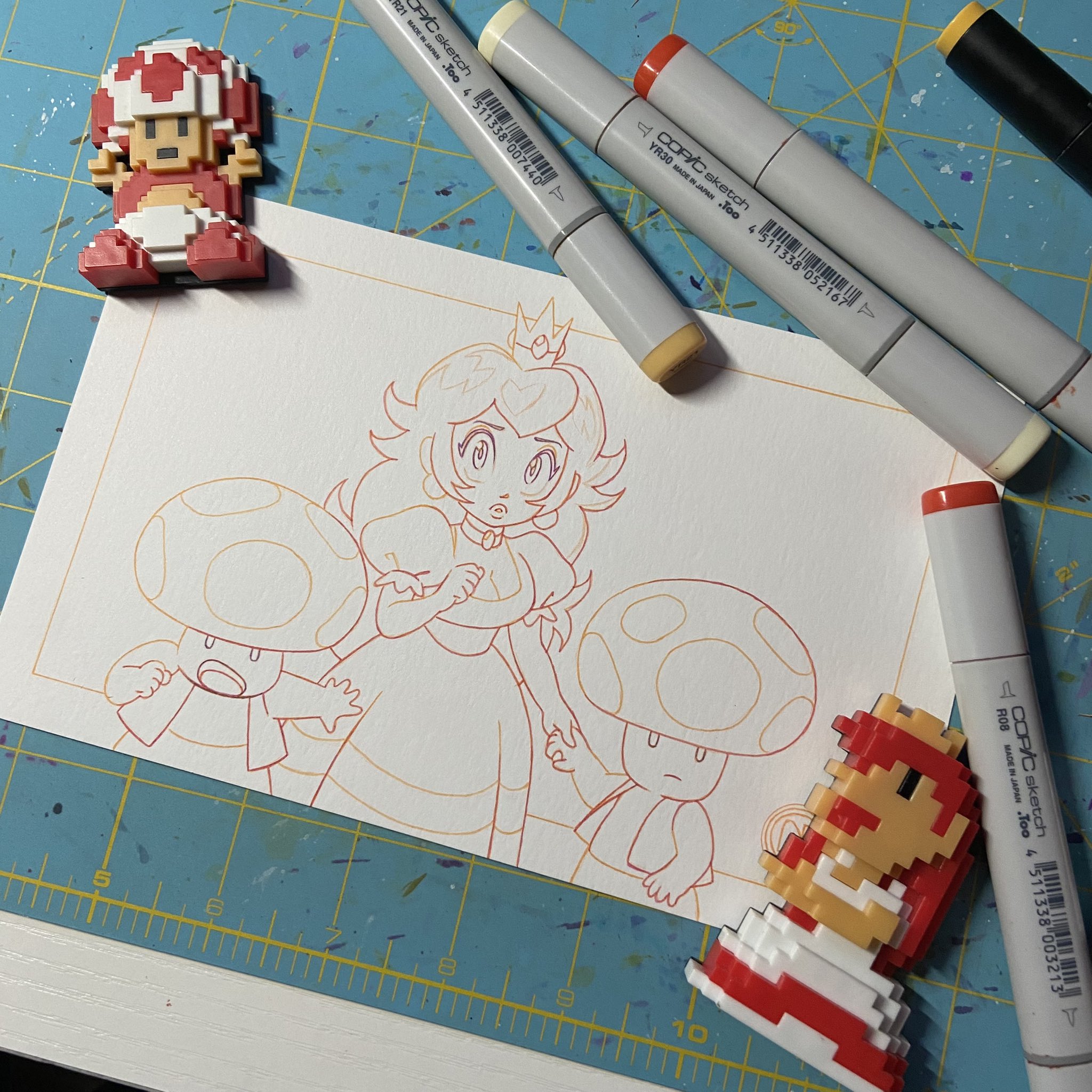 this is a drawing of a princess peach, a toad, and a mario character. it is a line drawing done in red and orange marker. there are a few copic marker pens in the background that may have been used to create the drawing. the drawing is on a white piece of paper that is laid out on a blue grid mat.