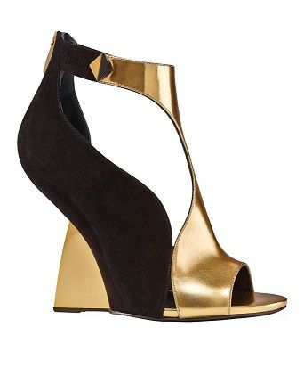closeup shot of a pair of women's designer sandals. the shoes feature a unique design with a black suede upper and gold leather accents.  they are wedge sandals with an open toe and a tstrap. the wedge heel is a gold metallic color.  the shoes appear elegant and stylish.