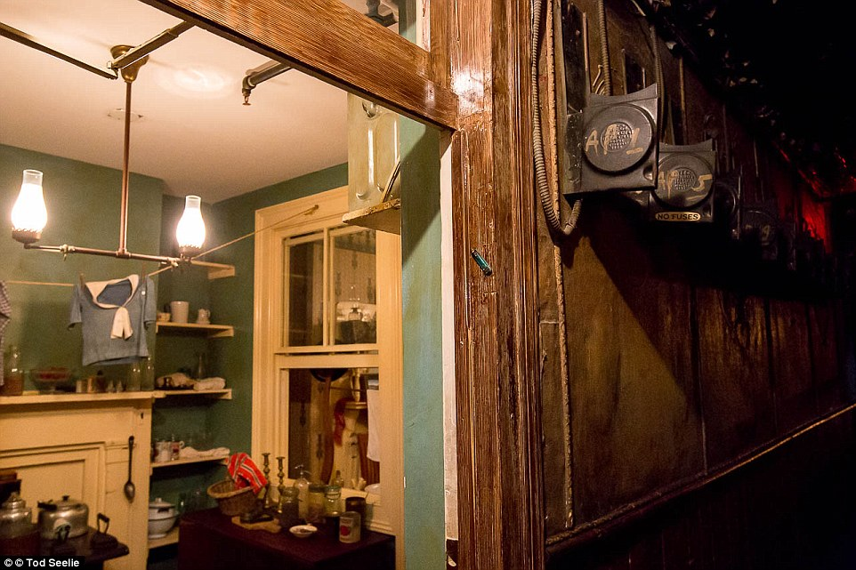 the image shows the doorway of what looks to be an old home. the doorway is made of wood and has a dark brown finish. there are clothes hanging on a clothesline in the kitchen. to the right of the door is a fuse box. the walls are painted a light green.
