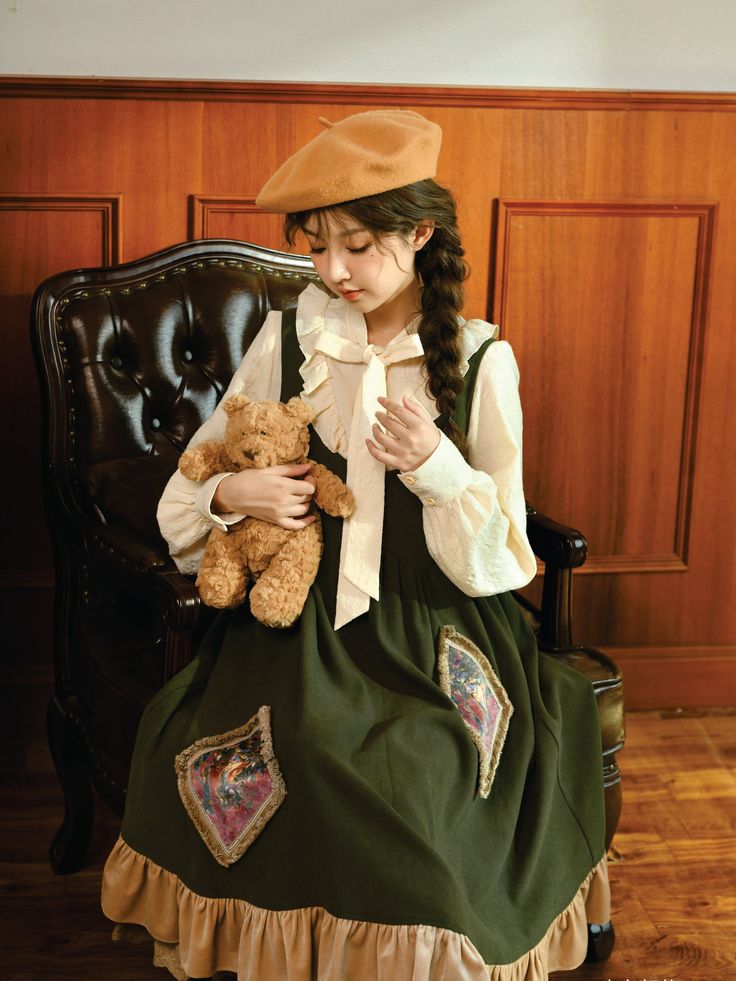 a young woman wearing a vintageinspired lolita fashion dress poses for a portrait. she is seated in a leather armchair and holds a teddy bear in her arms. the dress features intricate embroidery and lace details, and she complements the look with a matching beret. the warm, soft lighting enhances the vintage aesthetic of the image.