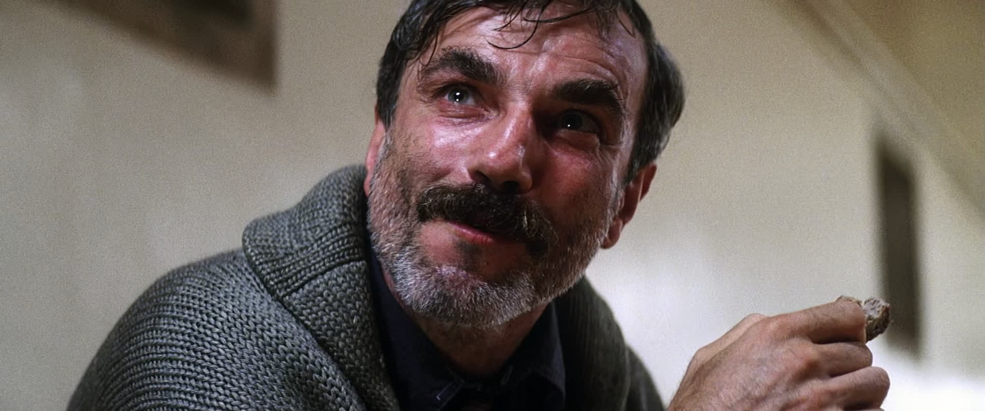 a closeup portrait of a man with a thick beard and mustache. he is looking thoughtfully towards the right side of the frame. he is wearing a gray sweater. the background is a light beige color. the man's expression is serious.  the lighting is soft and even.