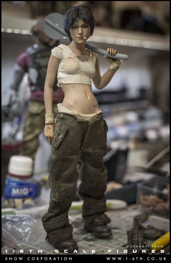 the image shows a highly detailed 1/6 scale action figure of a female character.  the figure has a weathered, postapocalyptic look, wearing dirty and worn combat fatigues and boots. she has a tattoo visible on her stomach and carries a circular saw blade across her shoulders as a weapon. the figure's pose is relaxed yet suggestive of a hardened and capable individual. the background shows a cluttered workshop setting, implying the figure is part of a collection or in the process of being photographed. the figure's high level of realism, particularly in the details of the clothing, skin, and overall sculpt, is evident. the watermark "odorgnal snow" and other information suggest it's a product from a specific maker or seller.