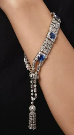 a closeup shot of a woman's wrist wearing a diamond bracelet with blue sapphires. the bracelet is fastened with a tassel that hangs down her arm. the bracelet sparkles in the light.