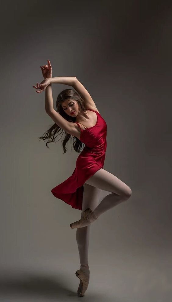 a captivating image of a ballerina in a flowing red silk dress, gracefully poised on pointe shoes against a muted grey backdrop.  her body is elegantly arched, showcasing her flexibility and control.  the lighting enhances the texture of her dress and the delicate details of her pointe shoes. the overall mood is artistic and serene, emphasizing the beauty and athleticism of ballet.