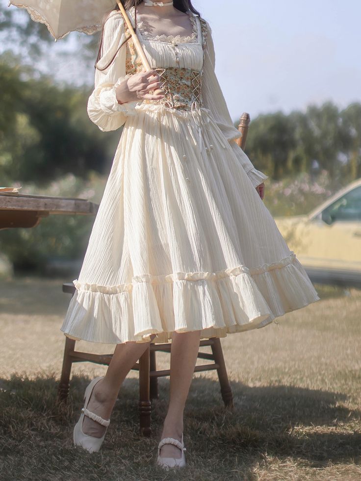 a woman in a long white dress stands in a field, holding a parasol. the dress has lace and embroidery details, and the skirt is full and flowing. the woman is wearing white shoes and her hair is styled in a simple updo. the overall look is romantic and ethereal.