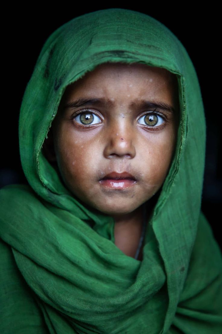a closeup portrait of a young girl with hazel eyes, wearing a green hijab against a dark background.