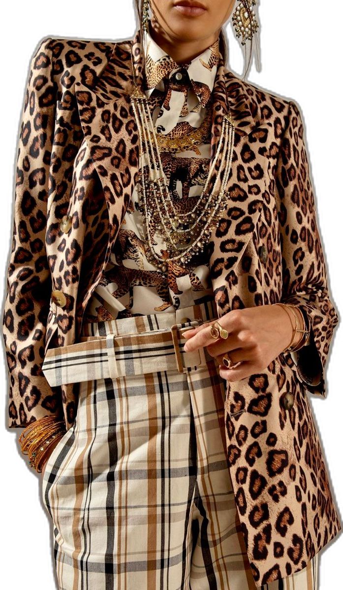 loseup view of a woman wearing a stylish outfit. she's wearing a brown and beige leopard print doublebreasted blazer over a creamcolored shirt with a leopard print design. the shirt is paired with beige and brown checked trousers.  she accessorizes with multiple gold necklaces, earrings, bracelets, and rings. the overall style is chic and fashionforward, blending animal print and plaid patterns.