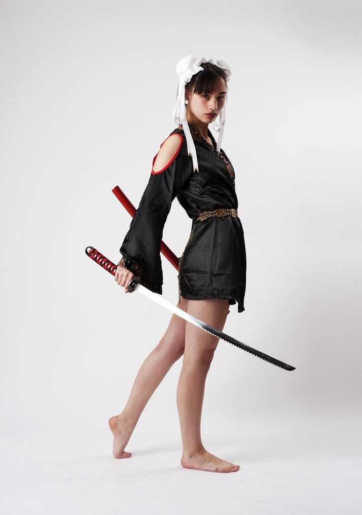 a woman in a black dress and a white headband holds a katana and looks intensely at something off camera.  she is standing on a white background.  she is striking a pose that makes her look powerful and fierce.