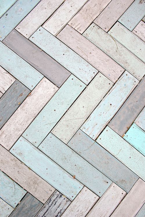 a closeup shot of a weathered wooden floor with a herringbone pattern. the planks are painted in shades of blue, white, and gray, and the paint is faded and distressed. the floor is very old and rustic, and has a very shabby chic look.