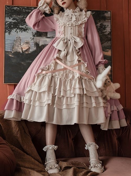 a young woman wearing an elaborate, vintageinspired pink and cream lolita fashion dress poses with a teddy bear. she is standing in front of a richly colored couch, with an ornate landscape painting hanging on the wall behind her. her dress features voluminous ruffles, delicate lace trim, a bow at the waist, and long sleeves with ruffled cuffs. she is also wearing white socks and pearlembellished heels.  the overall image evokes a sense of delicate femininity and romanticism.