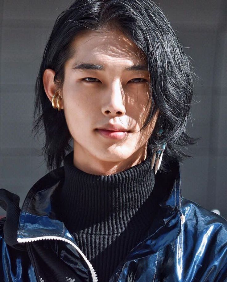 a portrait of a stylish asian man with medium length black hair and gold earrings. he is wearing a black turtleneck sweater and a shiny blue jacket. the man is looking directly at the camera with a neutral expression.