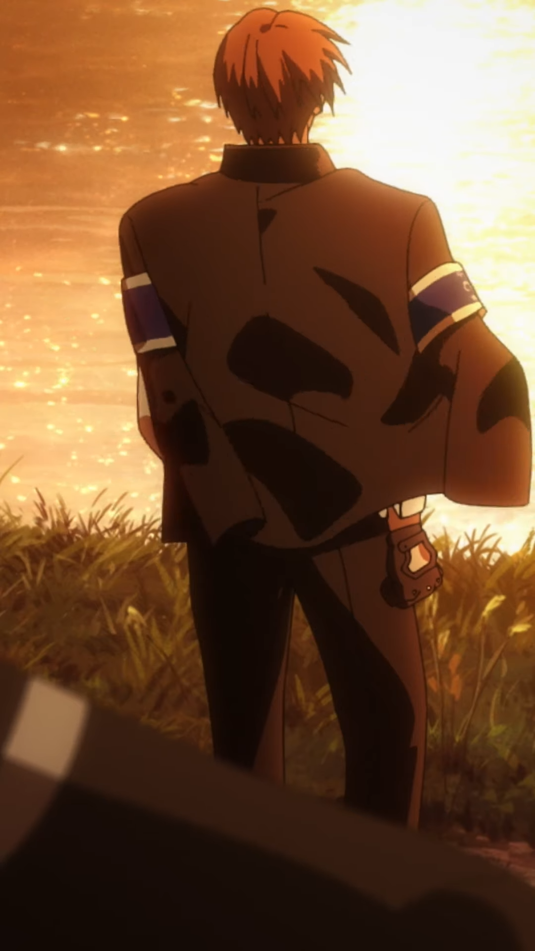 the image shows a man with short brown hair wearing a suit with blue armbands, standing with his back to the camera. he is looking towards a body of water reflecting the setting sun, which bathes the scene in a warm, orange glow. the foreground is slightly out of focus, suggesting the perspective is from someone else's point of view.