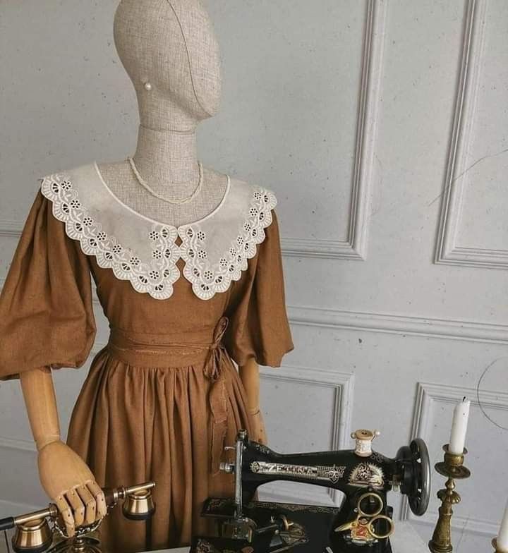 a mannequin is adorned in a vintageinspired brown dress featuring a delicate white lace collar.  the scene is set in a room with a vintage sewing machine and an antique telephone, hinting at a bygone era of fashion and craftsmanship.