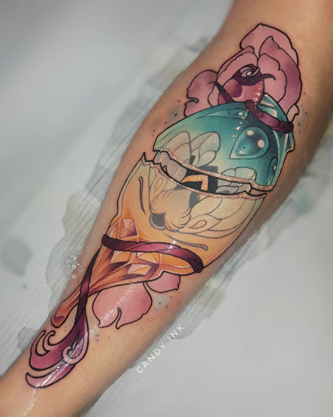 a neotraditional tattoo of a cracked open geode with a pink and yellow crystal inside, accented with pink roses and leaves. the tattoo is on someone's inner forearm.