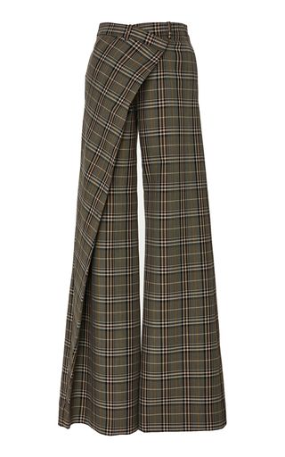 a pair of tan and brown plaid trousers is shown. one leg has a draped fabric layer over it, creating a fauxskirt effect.
