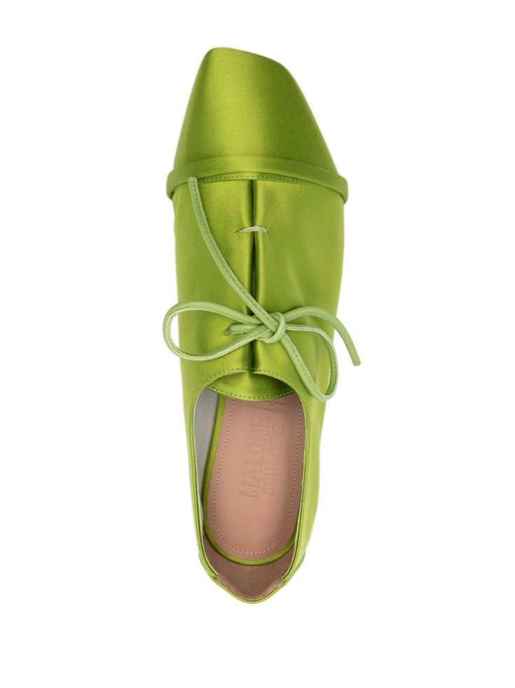 a topdown closeup shot of a pair of women's green satin flat shoes with a pointed toe. the shoes have a laceup detail across the vamp and a subtle sheen from the satin material. the insole is visible and is a light peach color.  the shoes look elegant and stylish.