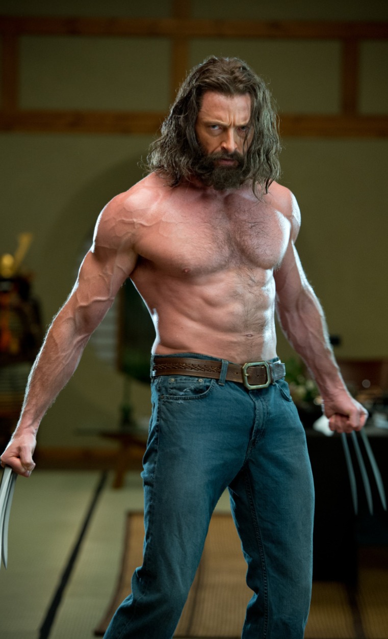 a full shot of hugh jackman as wolverine, shirtless with long hair and a beard, wearing jeans and a belt, with his claws extended.