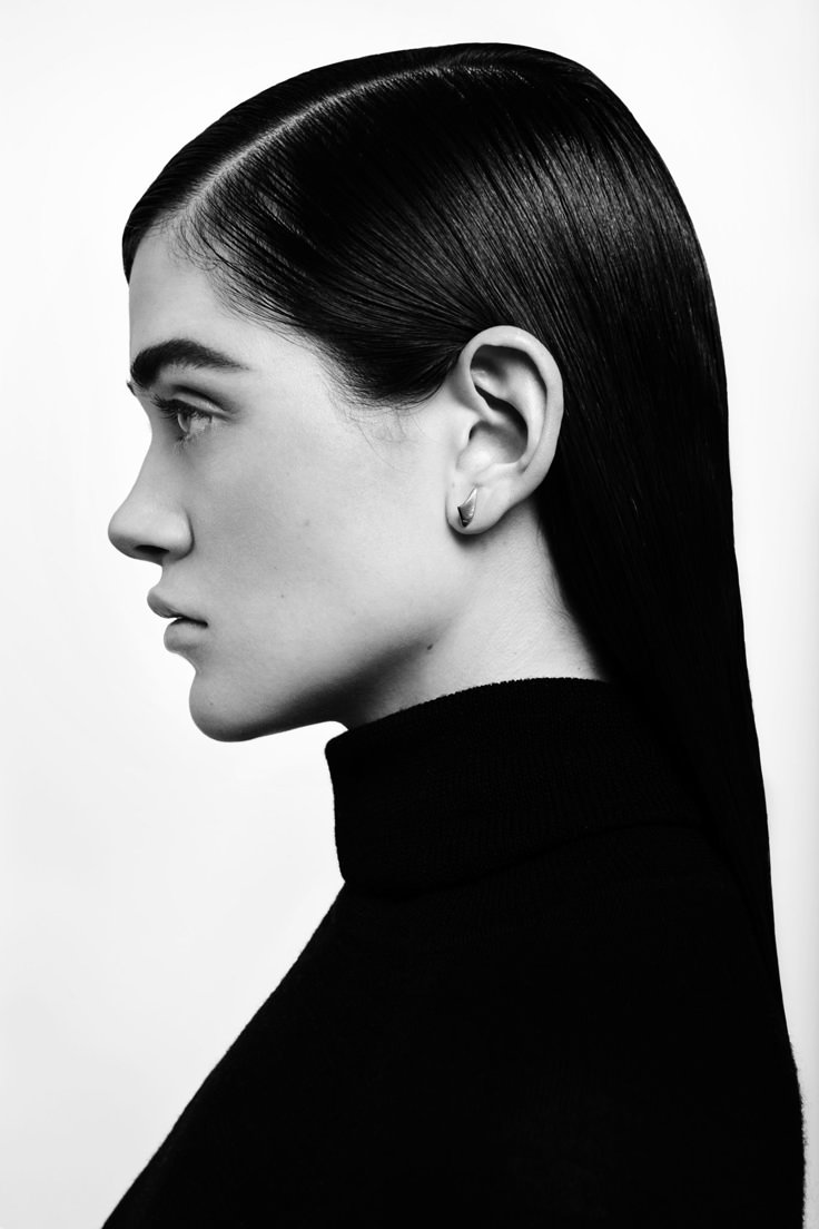 a black and white profile portrait of a woman wearing a black turtleneck. her hair is sleeked back, and she is wearing a small earring. the background is plain white.