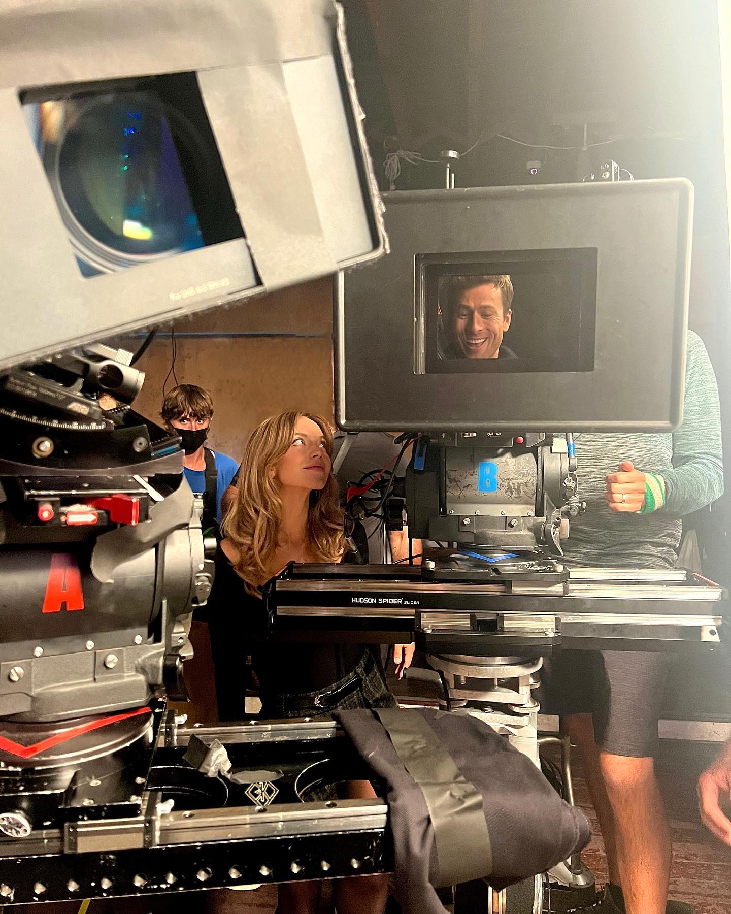 a behindthescenes photo from a film set. the image shows various pieces of filming equipment including a large camera and a monitor displaying ryan reynolds.  a woman with long blonde hair is standing to the side, and there are other crew members visible. the overall atmosphere suggests a professional movie production.