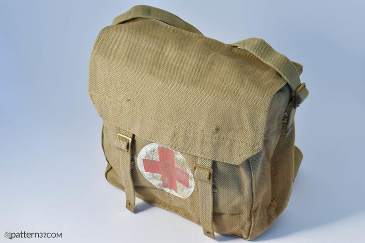 a khaki canvas first aid bag with a red cross on it. it has a strap and is vintage.
