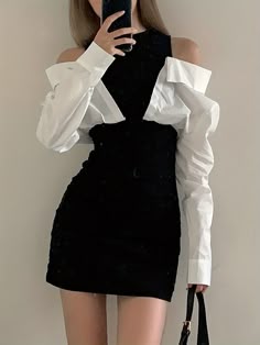 a woman is wearing a white offtheshoulder shirt and a black mini skirt. she is holding a phone in her hand and looking into the mirror. she is also carrying a black handbag.